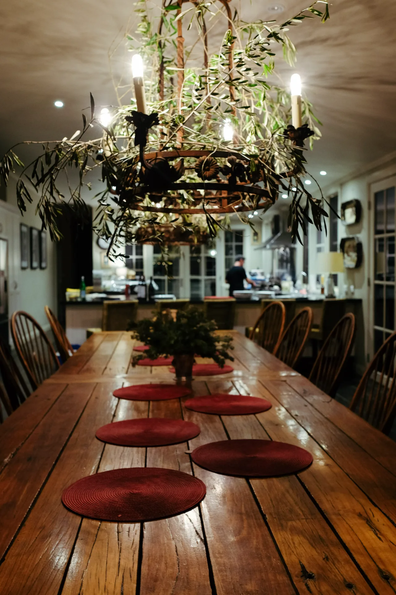 A long timber table set beneath a foliage canopy in the lodge kitchen.