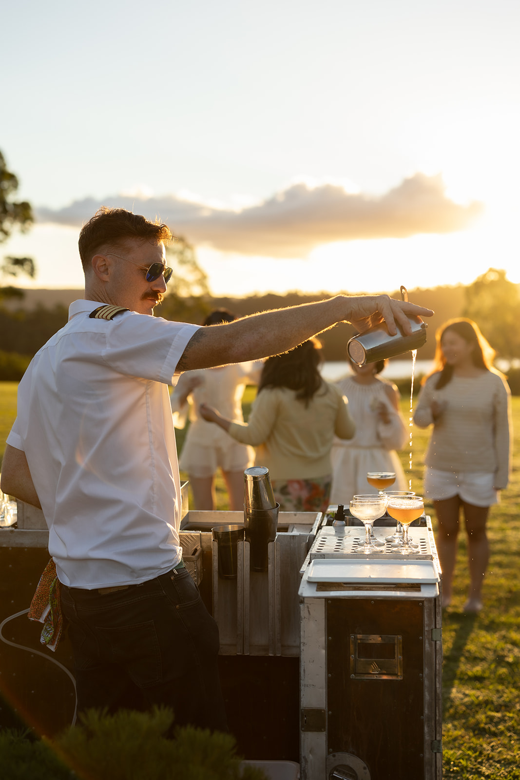 Byron Woolfrey pouring drinks at the bar as the sun goes down over the valley.