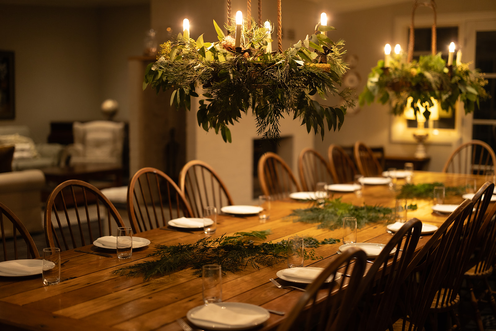 A long table set by candlelight beneath a hanging arrangement of native foliage.